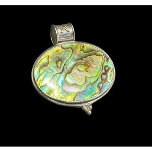May include: A silver pendant with an oval abalone shell inlay. The shell has iridescent green, blue, and gold colors. The pendant has a bail with a small cross engraved on it.