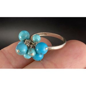 May include: A silver ring with a cluster of turquoise blue stones. The stones are attached to the ring with small silver chains.