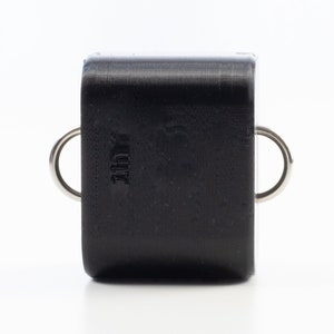 May include: Black rectangular key chain with two silver metal rings. The keychain has the word "JUI" embossed on the front.