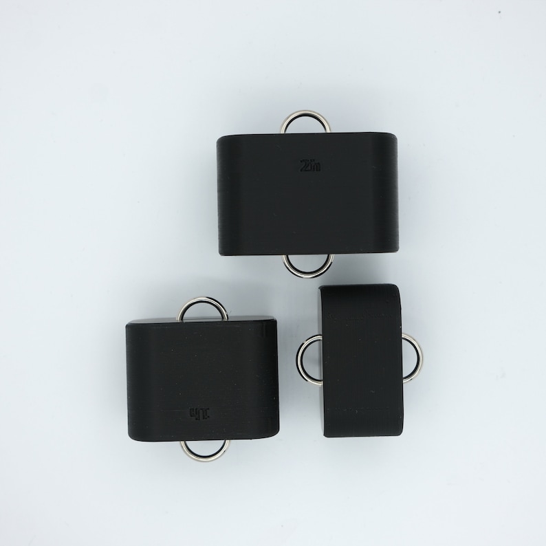 May include: Three black square-shaped weights with metal rings. The weights are labeled "25lb" and "30lb".