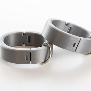 K&ouml;nnte beinhalten: Zwei silberne Metallringe mit einer Scharnier&ouml;ffnung und einer kleinen Metallschlaufe an jedem Ring.