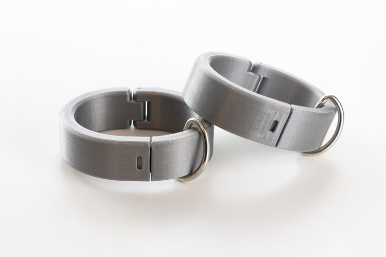 K&ouml;nnte beinhalten: Zwei silberne Metallringe mit einer Scharnier&ouml;ffnung und einer kleinen Metallschlaufe an jedem Ring.