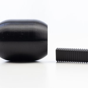 May include: Two black rubber weightlifting dumbbells with metal rings. The larger dumbbell is cylindrical and the smaller dumbbell is rectangular.