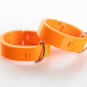 K&ouml;nnte beinhalten: Zwei verstellbare Ringe aus orangefarbenem Kunststoff mit silbernen Metallverschl&uuml;ssen und D-Ringen.