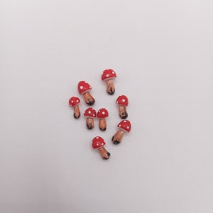 May include: A collection of eight small, hand-painted mushroom figurines. Each piece features a rounded red cap with white polka dots and a light brown stem with a darker brown base. The mushrooms are arranged in a loose cluster on a plain surface.