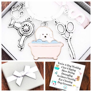 May include: A silver keychain with charms of a dog in a bath, a hairdryer, scissors, and a paw print. The keychain comes in a small gift box with a silver bow and a card that reads "You're A Dog Washing, Claw Clipping, Blow Drying, Detangling, Accident Cleaning, Ear Cleaning, Dog Groomer".