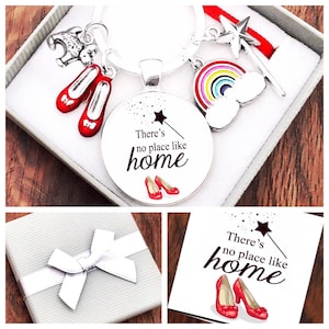 May include: A silver keyring with a round charm that says "There's no place like home" with red ruby slippers and a silver star wand. The keyring is in a white gift box with a silver bow.
