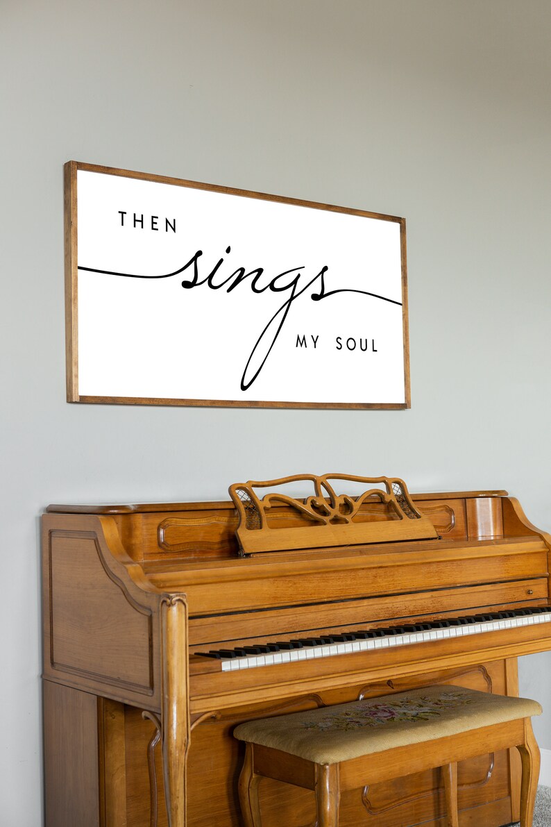 May include: A framed print with the text "Then sings my soul" in a cursive font. The print is hanging on a light grey wall above a wooden piano with a matching piano bench.