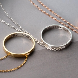 Könnte beinhalten: Drei personalisierte Ringketten in Gold, Silber und Roségold. Jeder Ring ist mit Text graviert und hängt an einer zarten Kette. Die Halsketten werden auf einer grauen Oberfläche präsentiert.