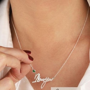 Op de afbeelding: Zilveren ketting met een 'Ik hou van je' hanger in cursief schrift en een klein groen edelsteentje.
