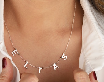 May include: A silver necklace with the name "ELIAS" spelled out in individual letters hanging from the chain.