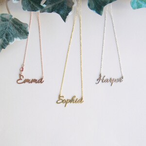 May include: Three gold necklaces with the names "Emma", "Sophia", and "Harper" hanging from them. The necklace with the name "Emma" is rose gold.