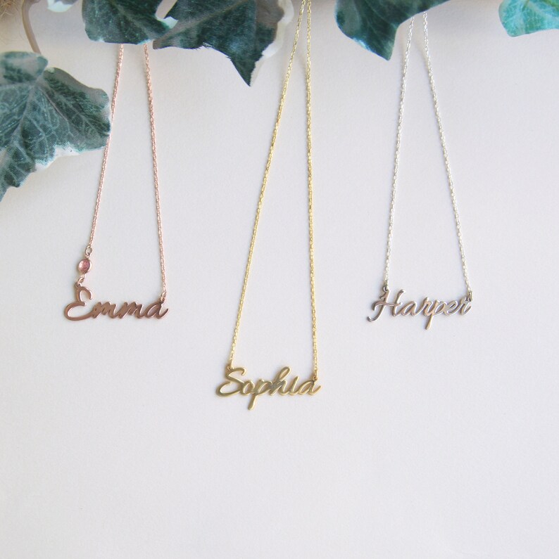 May include: Three gold necklaces with the names "Emma", "Sophia", and "Harper" hanging from them. The necklace with the name "Emma" is rose gold.