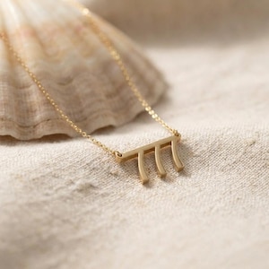 May include: A gold-colored necklace with a pendant featuring the number 777. The pendant is a horizontal bar with three vertical lines. The necklace is on a light-colored surface, with a seashell in the background.