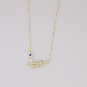 Op de afbeelding: Gouden ketting met een blauwe edelsteen en de woorden "Ik hou van je mama" in cursief.