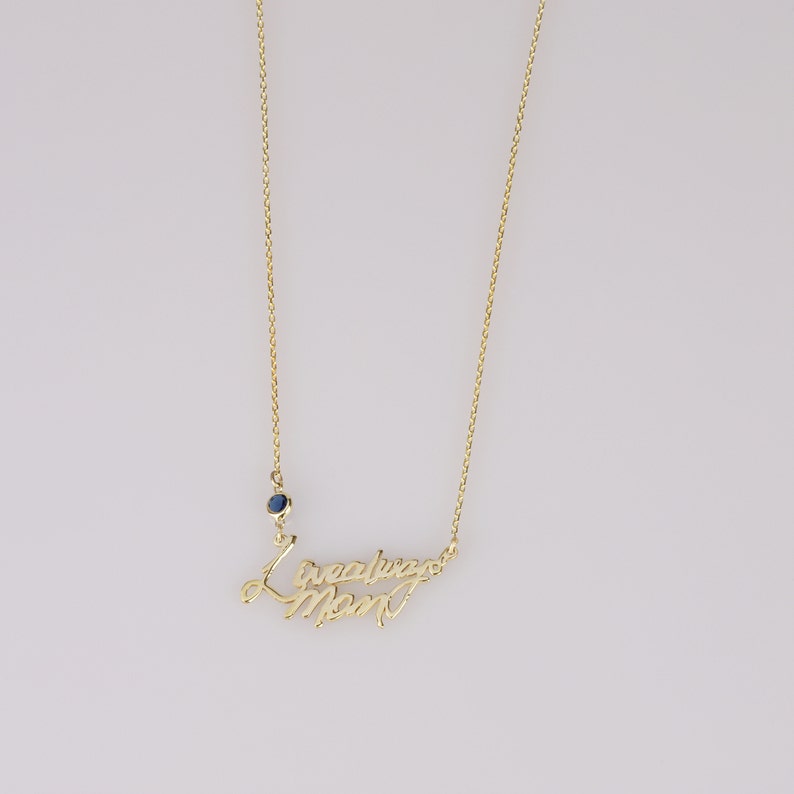 Op de afbeelding: Gouden ketting met een blauwe edelsteen en de woorden "Ik hou van je mama" in cursief.