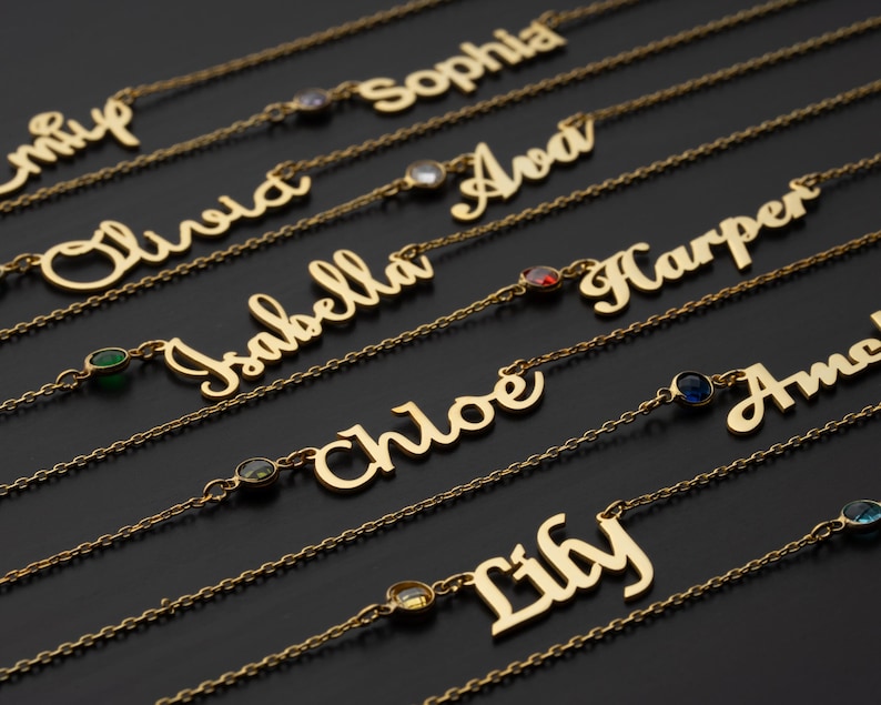a collection of gold-colored personalized name necklaces with gemstones. The necklaces have names engraved on them, such as "Sophia", "Oliver", "Ava", "Harper", "Isabella", " Chloe", "Lilly", and "Amanda". The necklaces are arranged in rows, showcasing their unique designs and the names on them.