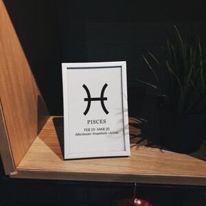 May include: A white framed print with a black Pisces zodiac symbol and the dates February 19 - March 20. The text "Pisces" and "Affectionate - Empathetic - Artistic" are also printed on the print.
