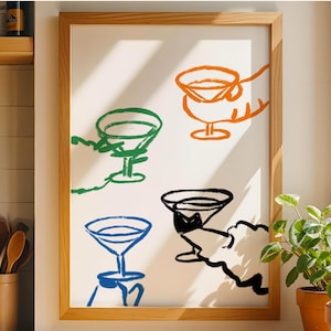 May include: A framed art print featuring four colorful cocktail glasses in green, orange, blue, and black. The minimalist design shows hands holding the glasses, creating a playful and modern aesthetic. The artwork is set against a white background.