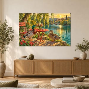 Op de afbeelding: Een rechthoekige wandkunstprint met een rivierlandschap bij zonsondergang. Twee wilde eenden staan bij een kleine rode metalen bistrotafel en stoel. Er staat een vaas met bloemen op de tafel, met een brug en bomen op de achtergrond.