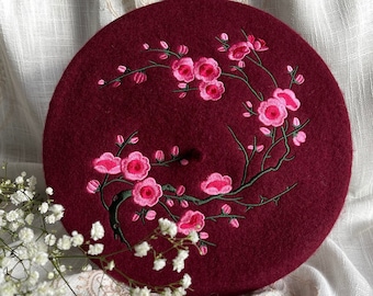 May include: A burgundy beret with a delicate embroidered design of pink flowers and green leaves.