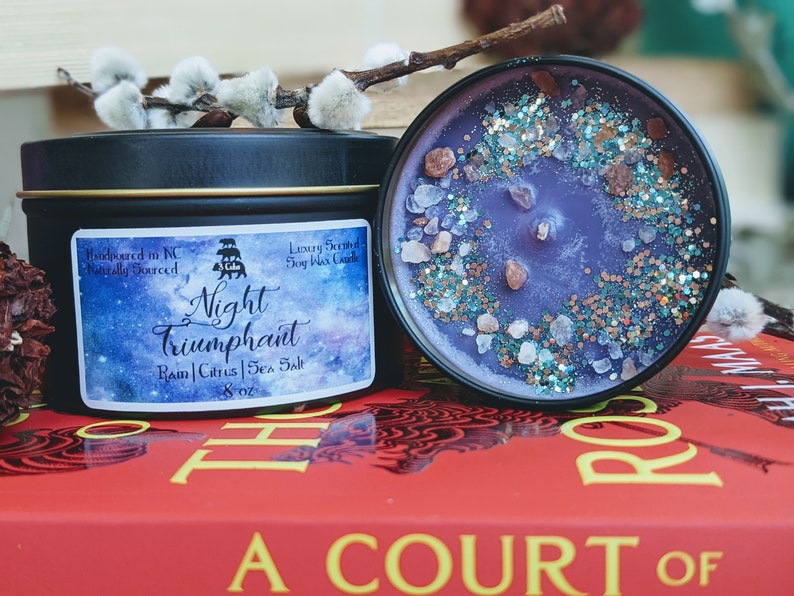May include: A black tin candle with a purple soy wax candle inside. The candle is decorated with sea salt and glitter. The label on the candle says "Night Triumphant Rain | Citrus | Sea Salt 8 oz".