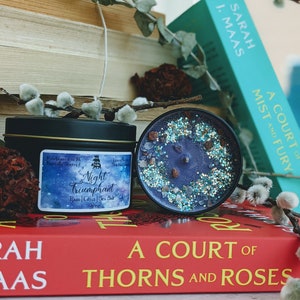 May include: A black candle jar with a purple wax and glitter on top. The candle jar has a label that reads "Night Triumphant" with the scent notes "Ram, Citrus, Sea Salt". The candle jar is sitting on top of a red book with the title "A Court of Thorns and Roses".
