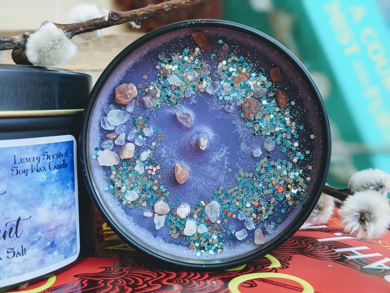 May include: Purple soy wax candle with a glittery, sparkly finish. The candle is topped with small pieces of pink and white rock salt. The candle is in a black tin with the text "Luxury Scented Soy Wax Candle" and "Salt" on the label.
