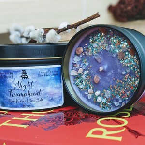 May include: A purple soy wax candle in a black tin with a galaxy design. The candle is labeled "Night Triumphant" and has a scent of Rain, Citrus, and Sea Salt. The candle is 8 oz.