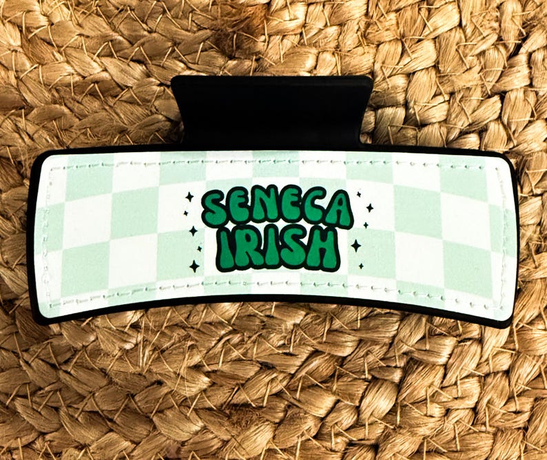 K&ouml;nnte beinhalten: Ein gr&uuml;ner und wei&szlig;er karierter Haarklammer mit dem Text "SENECA IRISH" in gr&uuml;nen Buchstaben.