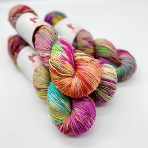 以下が含まれることがあります： ピンク、オレンジ、イエロー、グリーン、ブルーの色合いのカラフルな糸が3玉。糸はボール状に巻かれており、斑点模様になっています。