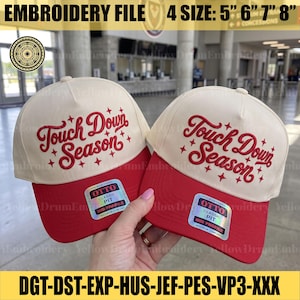 Op de afbeelding: Twee crèmekleurige baseballpetten met rode kleppen, voorzien van rode geborduurde tekst Touch Down Season omringd door kleine sterren. Elke pet heeft een holografische Otto Classic Fit-sticker op de klep, verkrijgbaar in de maten 5, 6, 7 en 8 inch.