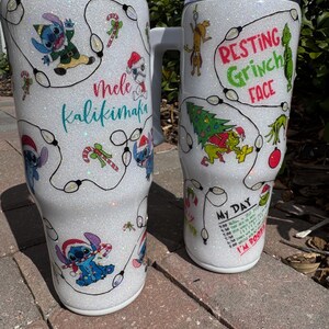Pu&ograve; includere: Due tazze da viaggio bianche glitterate con disegni a tema festivo. Una tazza presenta Stitch con il testo "Mele Kalikimaka", l'altra ha un tema Grinch con il testo "Resting Grinch Face" e un programma giornaliero. Entrambe le tazze hanno un manico.