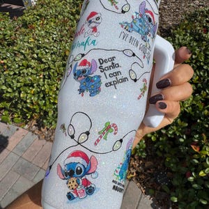 Pu&ograve; includere: Un bicchiere bianco glitterato con disegni di personaggi dei cartoni animati festivi, tra cui cappelli di Babbo Natale e luci natalizie. Il bicchiere mostra le frasi "Dear Santa, I can explain" e "I've been good-ish". Sono presenti anche bastoncini di zucchero e altri disegni natalizi.