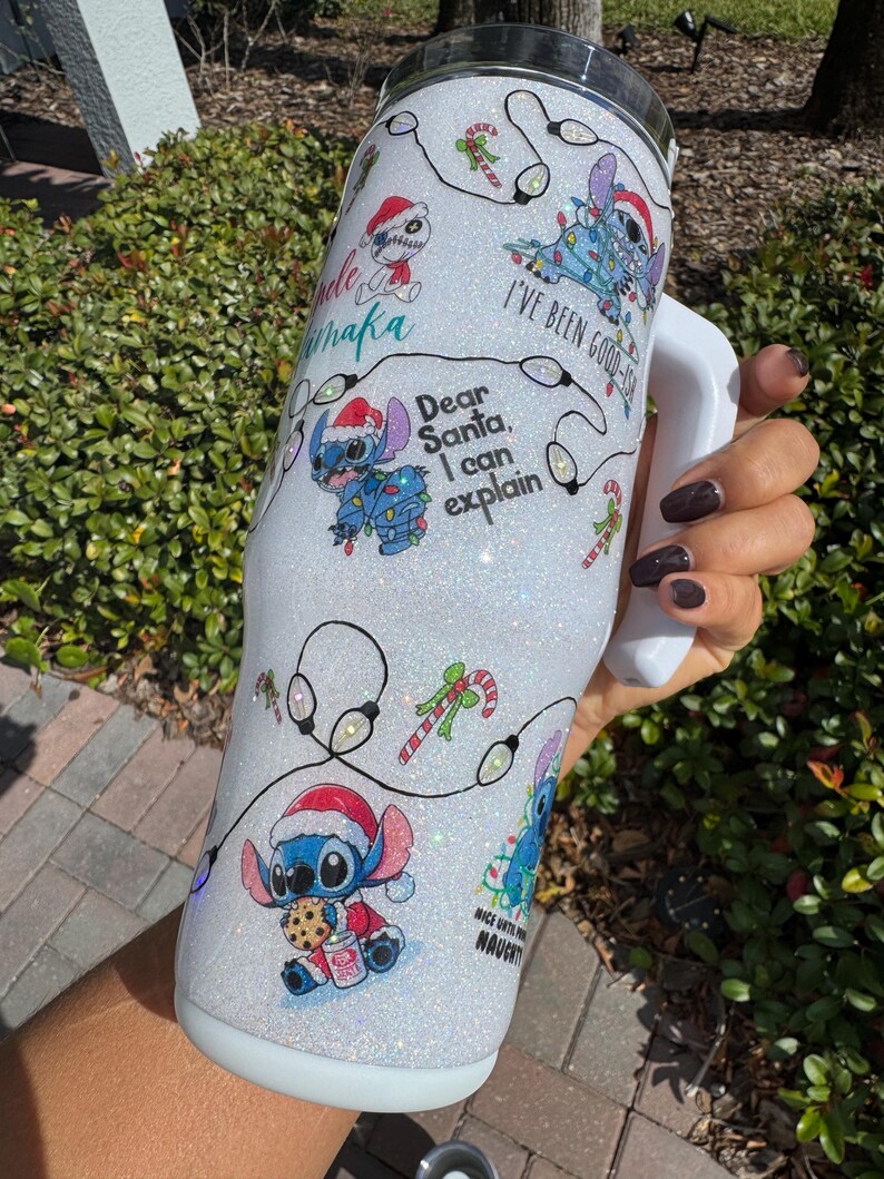 Pu&ograve; includere: Un bicchiere bianco glitterato con disegni di personaggi dei cartoni animati festivi, tra cui cappelli di Babbo Natale e luci natalizie. Il bicchiere mostra le frasi "Dear Santa, I can explain" e "I've been good-ish". Sono presenti anche bastoncini di zucchero e altri disegni natalizi.