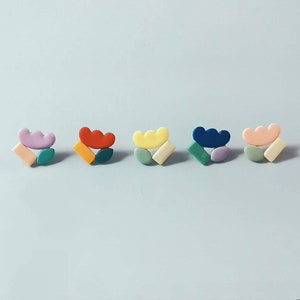 May include: Five pairs of colorful geometric earrings. Each pair features a different color combination of pink, red, yellow, blue, and peach.