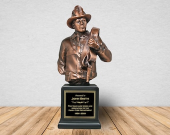 May include: A bronze bust of a firefighter holding a hose, mounted on a black base with a gold plaque that reads "Presented to JOHN SMITH For your hard work and dedication to the EAGLE FIRE DEPARTMENT 1990-2020"