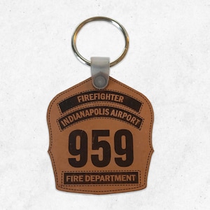 May include: Brown leather firefighter keychain with a silver key ring. The keychain features the text "Firefighter Indianapolis Airport 959 Fire Department".