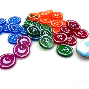 May include: A selection of colourful game tokens. The tokens are in various colours, including blue, orange, green, red, and purple. Some tokens have symbols like anchors, moons, and stars. Others have numbers. A single token features a world map.