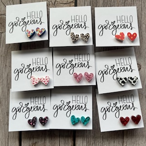 May include: Nine pairs of heart-shaped earrings with various patterns, including floral, animal print, and glitter. Each pair is displayed on a white card with the text "HELLO gorgeous".