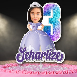 Puede incluir: Un adorno para tarta con una ilustración de dibujos animados de una niña con un vestido de princesa morado, una tiara y el número 3. El nombre "SCharlize" está escrito en morado. El adorno está sobre una tarta rosa con decoraciones de perlas blancas.