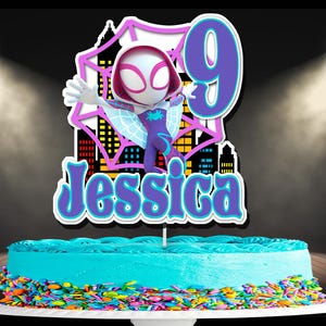 Könnte beinhalten: Ein Geburtstagskuchen mit blauer Glasur und bunten Streuseln. Der Kuchen ist mit einem Spider-Gwen-Kuchenaufsatz mit dem Namen "Jessica" und der Zahl "9" verziert. Im Hintergrund eine Stadtlandschaft.