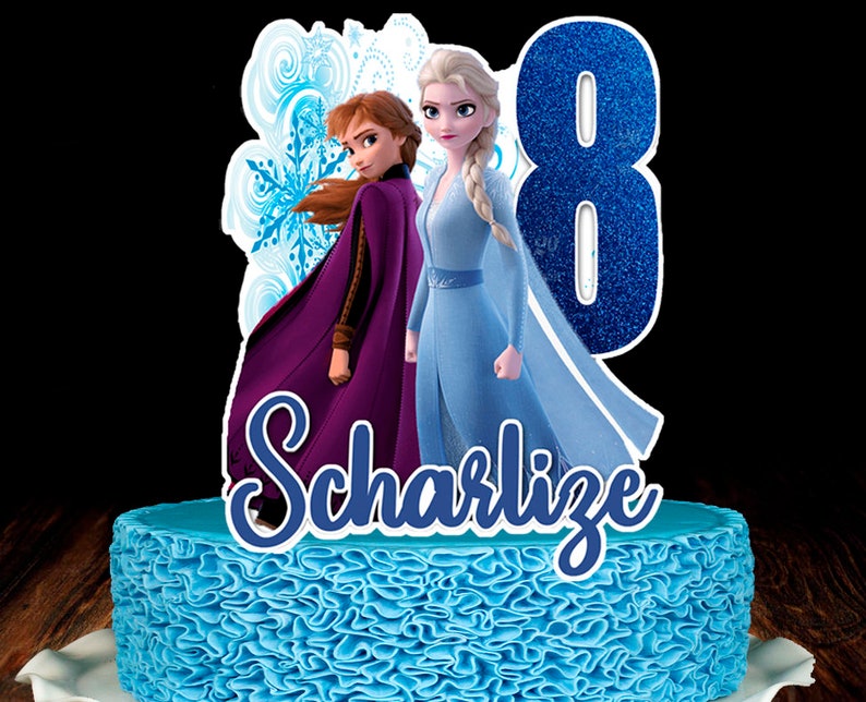 Op de afbeelding: Een blauwe taart met een gerimpeld frostingontwerp, bekroond met een decoratieve afbeelding van de Frozen-personages Anna en Elsa, het nummer 8 en de naam "SCharlize". De taart staat op een houten oppervlak.