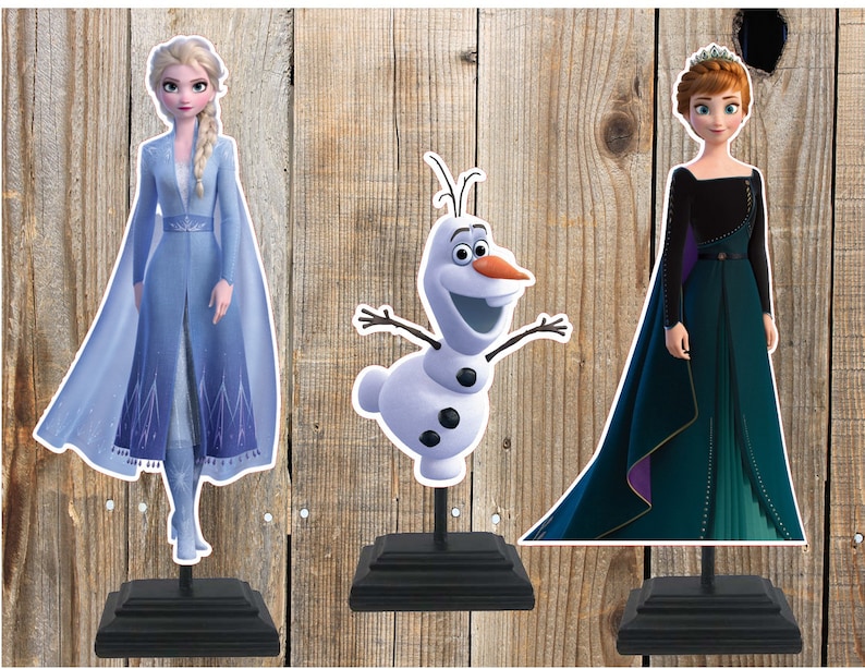 K&ouml;nnte beinhalten: Drei Pappfiguren von Charakteren aus dem Film Frozen. Die Figuren sind Elsa in einem blauen Kleid, Anna in einem gr&uuml;nen Kleid und Olaf der Schneemann.