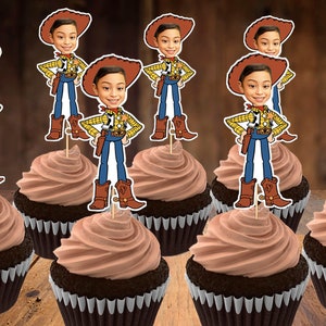 May include: Cupcakes with chocolate frosting and cowboy-themed toppers. The toppers feature a cartoon cowboy with a brown hat, yellow shirt, blue pants, and brown boots. The cupcakes sit on a wooden surface.