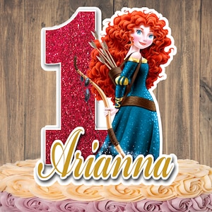 May include: A cake topper featuring a cartoon illustration of a princess with red curly hair, holding a bow and arrows, next to a glittery red number one. The name "Arianna" is written in gold script.