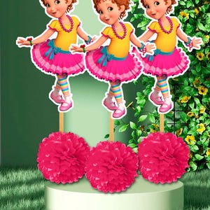 May include: Three-dimensional cutouts of a cartoon girl in a yellow top and pink tutu, with a pink necklace and a gold crown. Below are three large, pink paper pom-poms. The background is a green gradient with foliage.