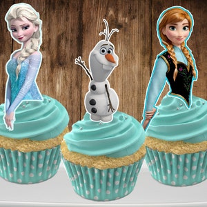 May include: Three cupcakes decorated with Frozen characters. The cupcakes have light blue frosting and white polka dot liners. The characters are Elsa, Anna, and Olaf.
