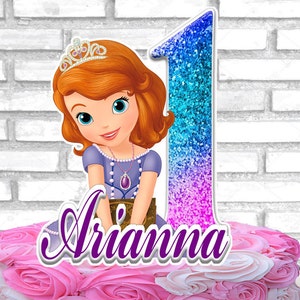 Puede incluir: Un adorno para pastel con una princesa de dibujos animados con una tiara y el número 1 en purpurina azul. El nombre "Arianna" está escrito en escritura morada. El pastel tiene glaseado rosa y blanco.