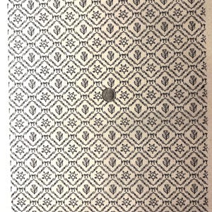 May include: Cream-coloured paper featuring a repeating black pattern of flowers, tulips, and bows. The design is arranged in a grid, creating a symmetrical and ornate appearance. A coin is placed on the paper for scale.